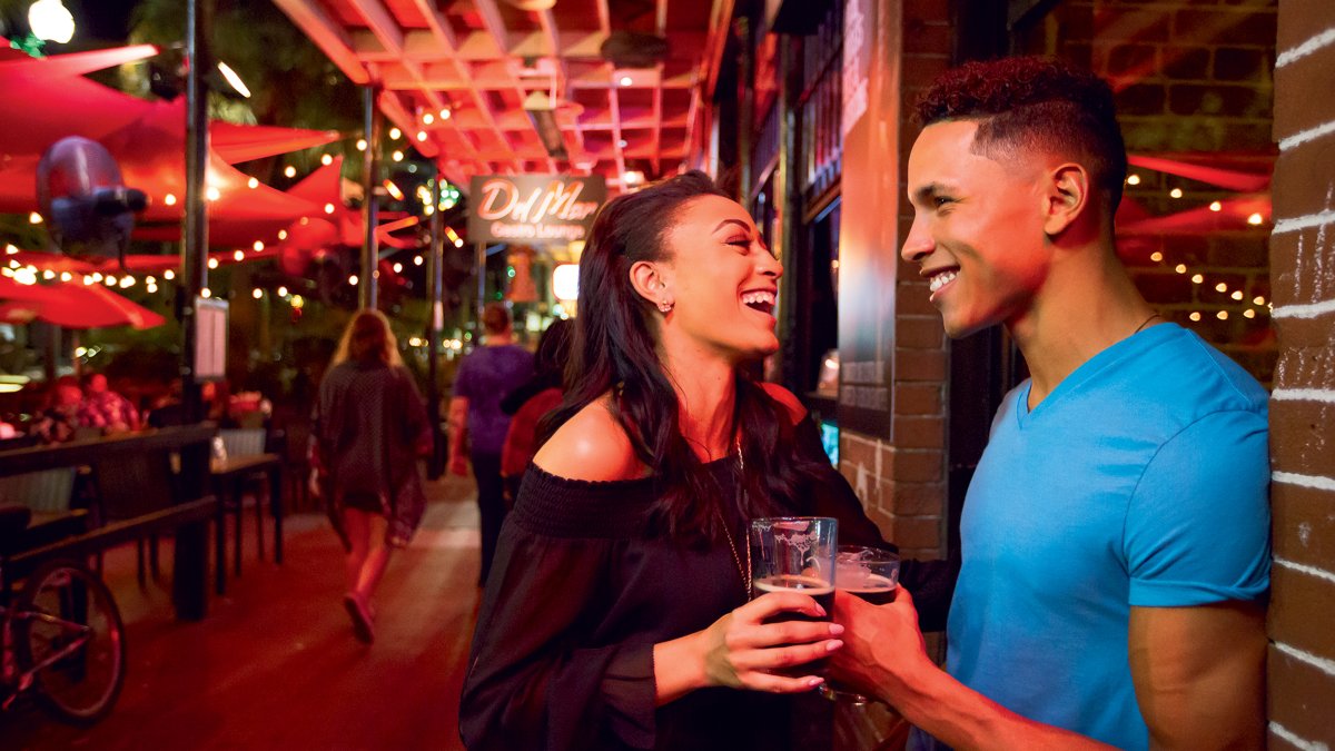 A couple enjoying drinks while standing against the brick facade of Del Mar Lounge in St. Pete.