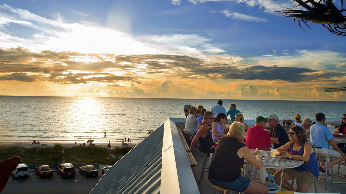 Menschen speisen bei Sonnenuntergang auf dem Dach einer Rooftop-Bar
