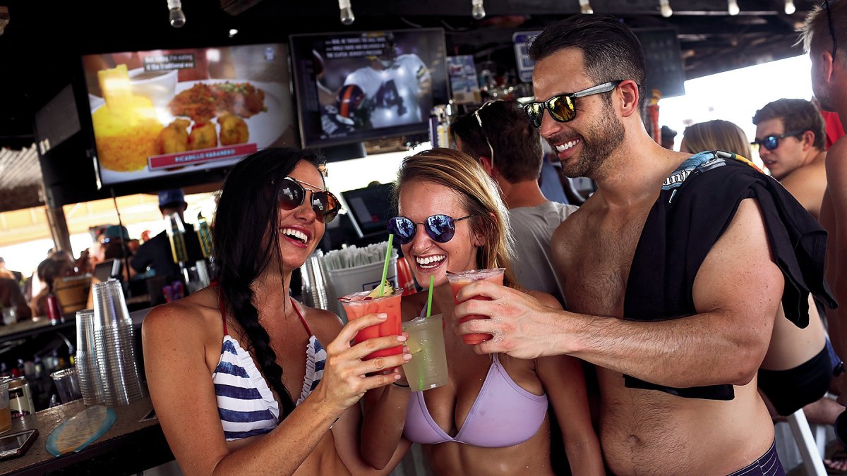 Três adultos brindam em trajes de banho no Post Card Inn em St. Pete Beach