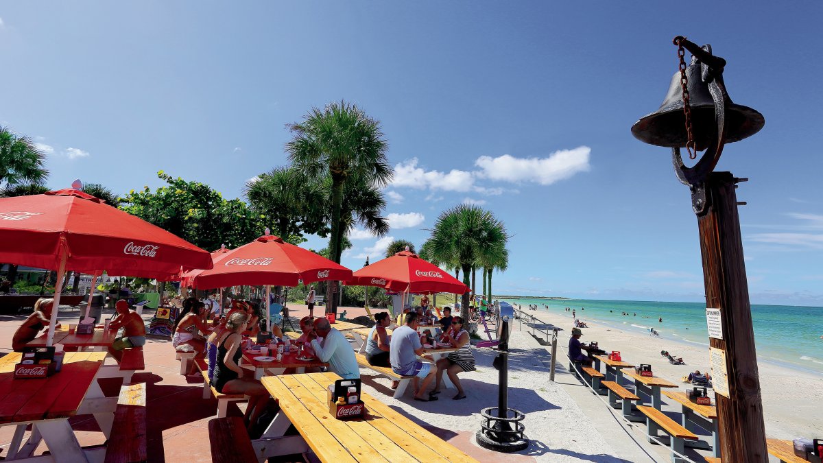 Menschen speisen draußen im Paradise Grille mit Blick auf den Strand von Pass-A-Grille