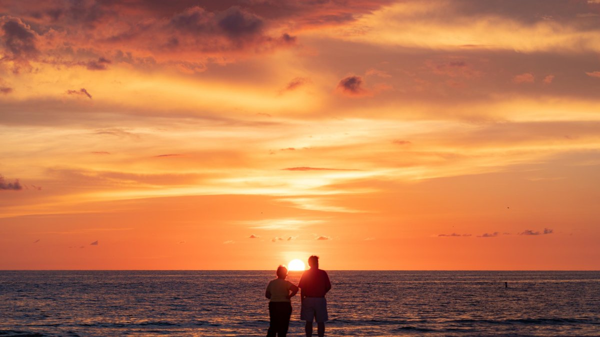 A couple stands on Pass-A-Grille Beach as the sun sets