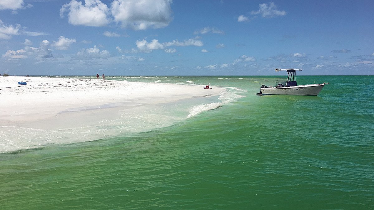 A boat anchored near the shore in Caladesi Island. A couple is seen at a distance.