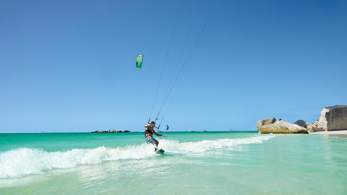 A man kitesurfing off Egmont Key. The water is emerald green with small waves and the ruins of Fort Dade can be seen.