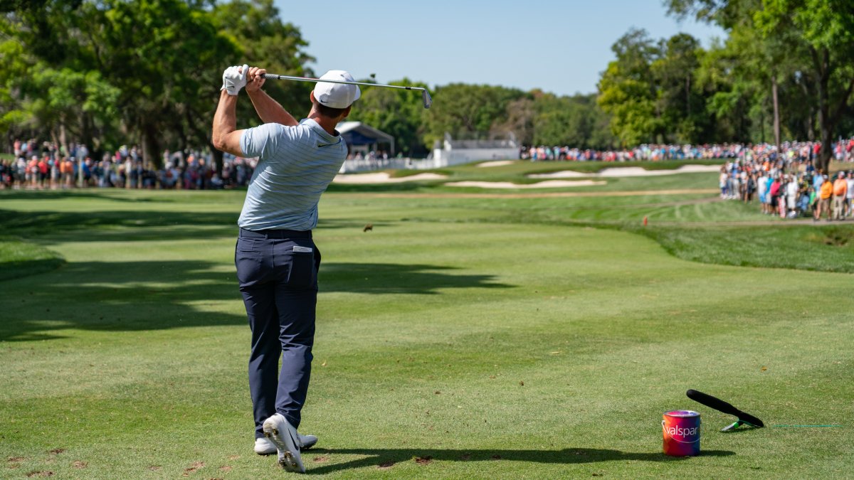 A golfer right after hitting the ball. A large crowd can be seen at a distance.