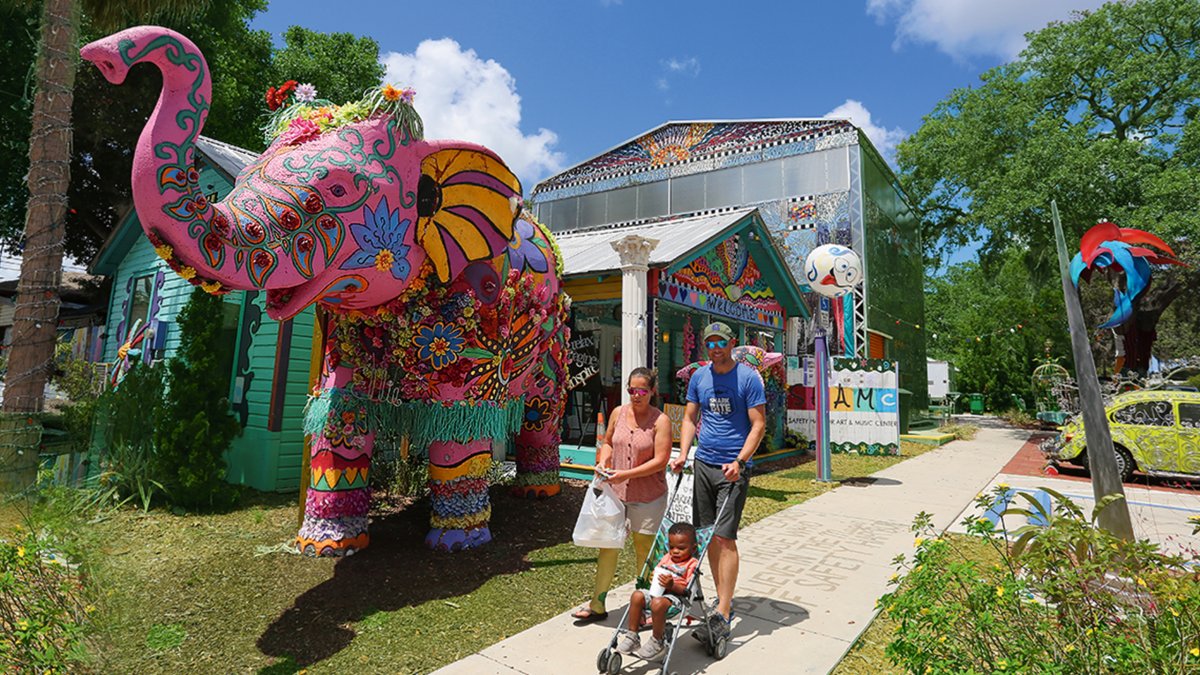 A couple strolling with a child in front of the pink elephant in front of the Safety Harbor Art & Music Center