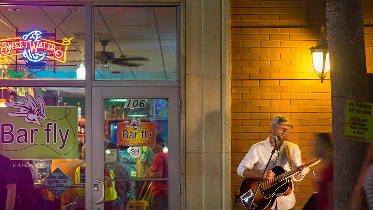 A musician playing guitar and singing outside of the Bar Fly in Safety Harbor at night.