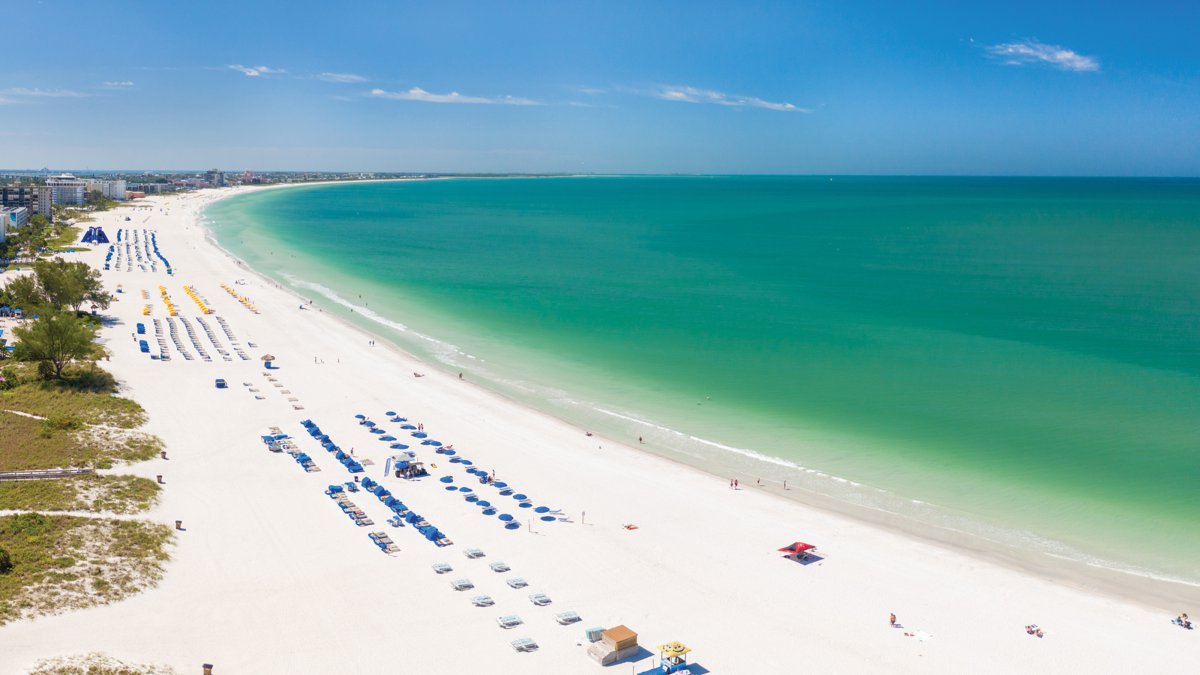 St. Pete Beach aerial panoramic photo showing the entire green waters beach, white sand and lots of hotels cabanas.