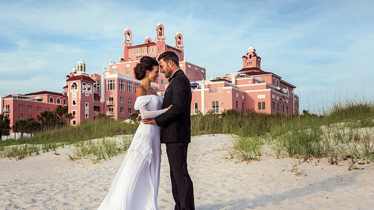 A couple hugging each other posing in front of Don Cesar for their wedding.