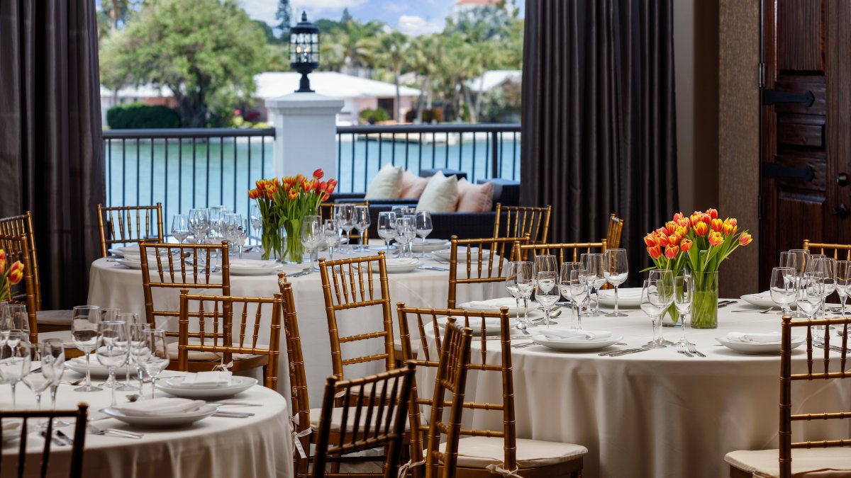 An indoor wedding reception room decorated with orange flowers with a view for the water.