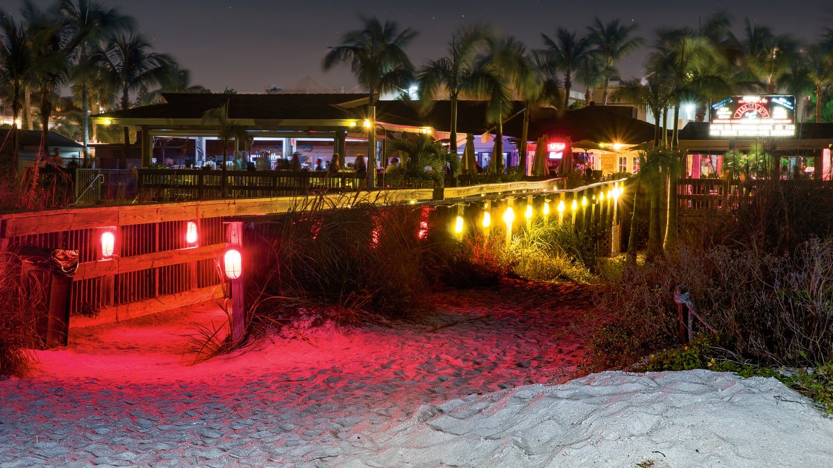 Uma visão noturna do bar de praia Jimmy B's, iluminado com luzes vermelhas.