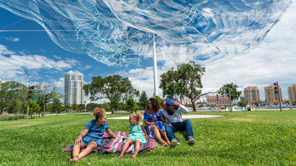 A family enjoying themselves in the grass field under the Echelman Sculpture at the St. Pete Pier.