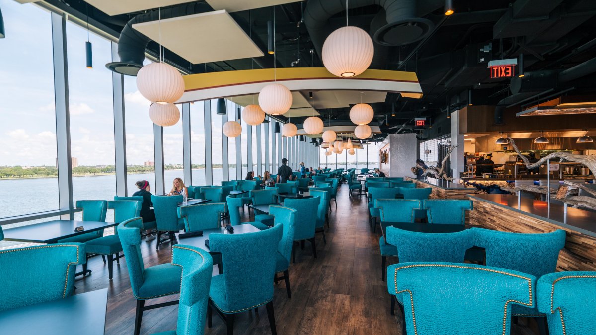 Aquamarine blue chairs and round chandeliers inside of Teak restaurant. Some people and servers are present.