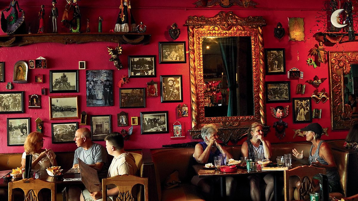 Six dinners eating at Casa Tina restaurant in Dunedin. The wall is red and decorated with multiple portraits.