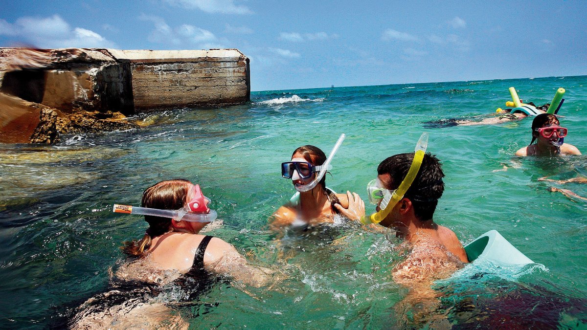 Eine Gruppe schnorchelt im klaren, blaugrünen Wasser neben einer Festung.