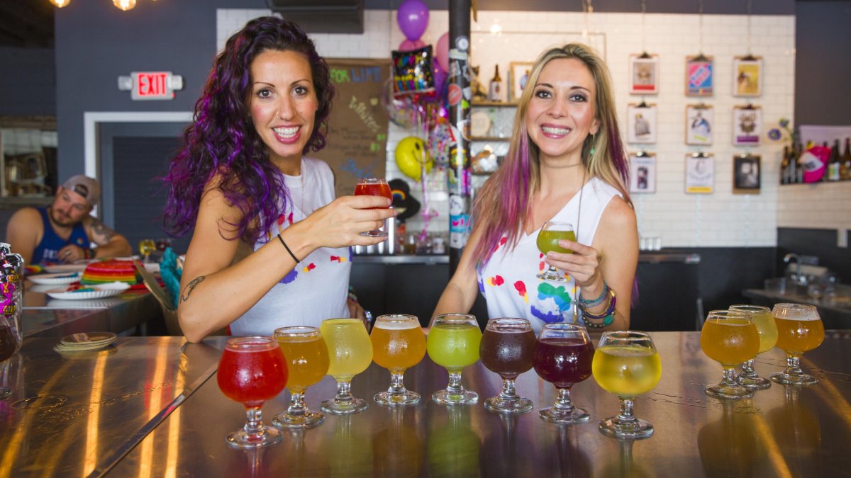 Two servers hold up a beer in front of more beer at Hawthorne Bottle Shop