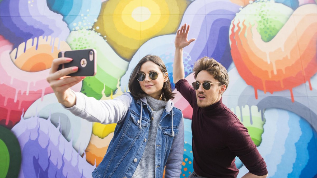 Duas pessoas tiram selfie em frente a um mural na quadra 600 da Avenida Central