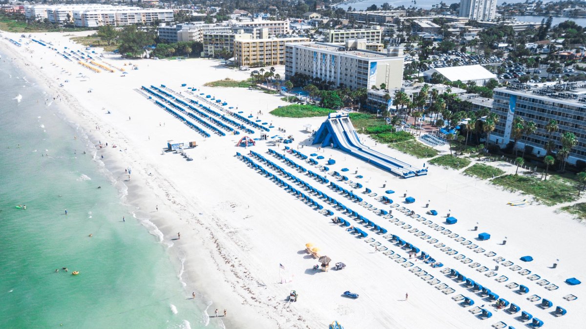 Arial View of St Pete Beach and Trade Winds Hotel, lines of beach chairs and giant blow up slide on the beach. 