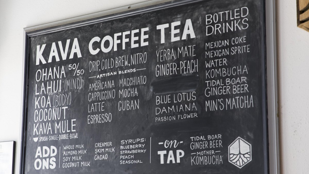 Picture of black chalk board on a wall with KAVA COFFEE TEA in bold and a menu filling the rest of the board against a white wall