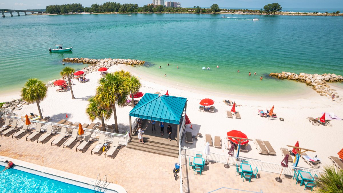 Arial view of pool side that walks into a beach on the Intracoastal Waterway, with beach chairs and palm trees.