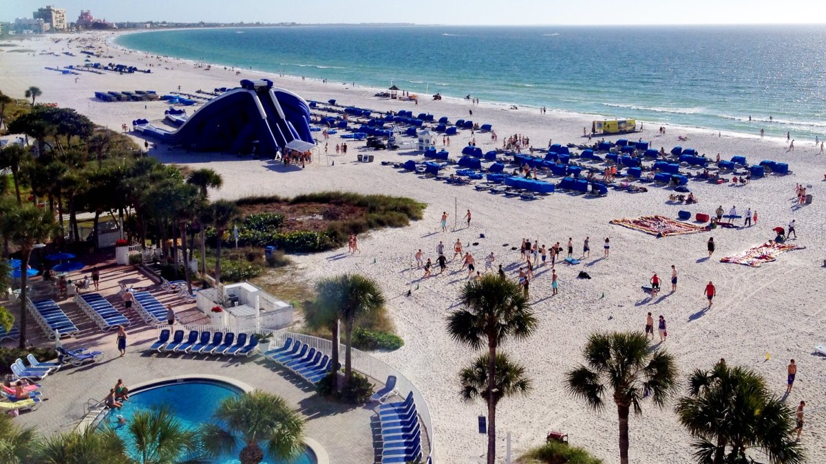 Arial view of Tradewinds Hotel Showing the pool by the beach, beach chairs lined on the beach and there iconic giant blowup slide.