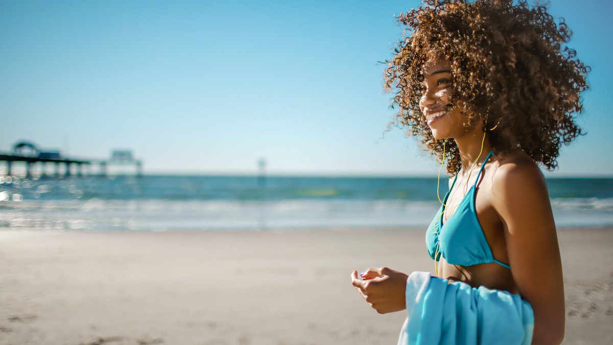 A woman on Clearwater Beach stands and smiles away from camera with Pier 60 in the background