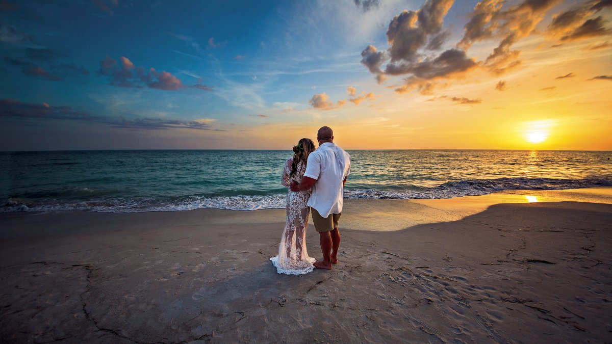 Bride and groom hugging each other and watching the sunset at the beach.