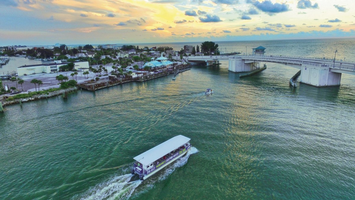 An overview of John's Pass during sunrise. A fishing boat is passing going by.