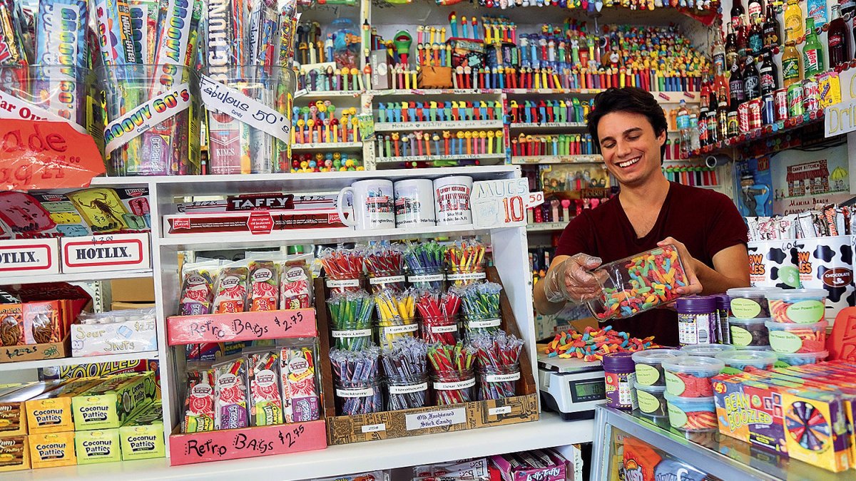 Um jovem cercado por muitos doces em exposição na loja Candy Kitchen.