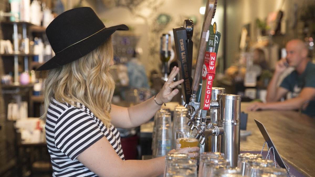 A lady wearing a black hat pouring beer from the draft.