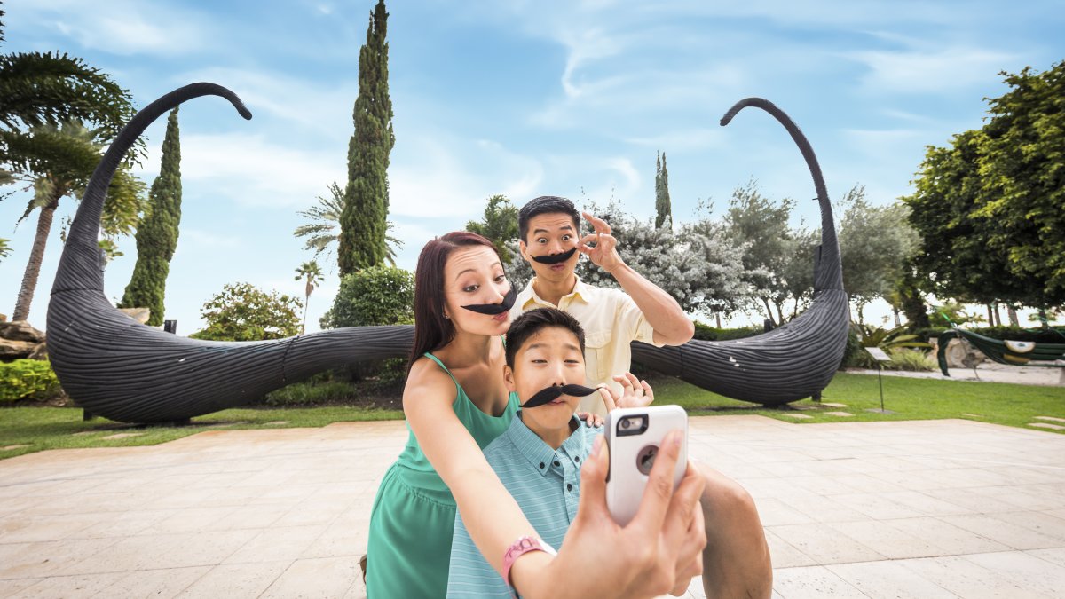 An Asiatic family wearing fake mustaches taking a selfie in front of the famous mustache sculpture at the Dali museum in St. Pete.