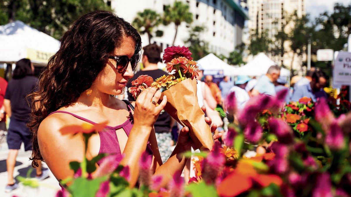 A young lady wearing sunglasses smelling flowers on display.