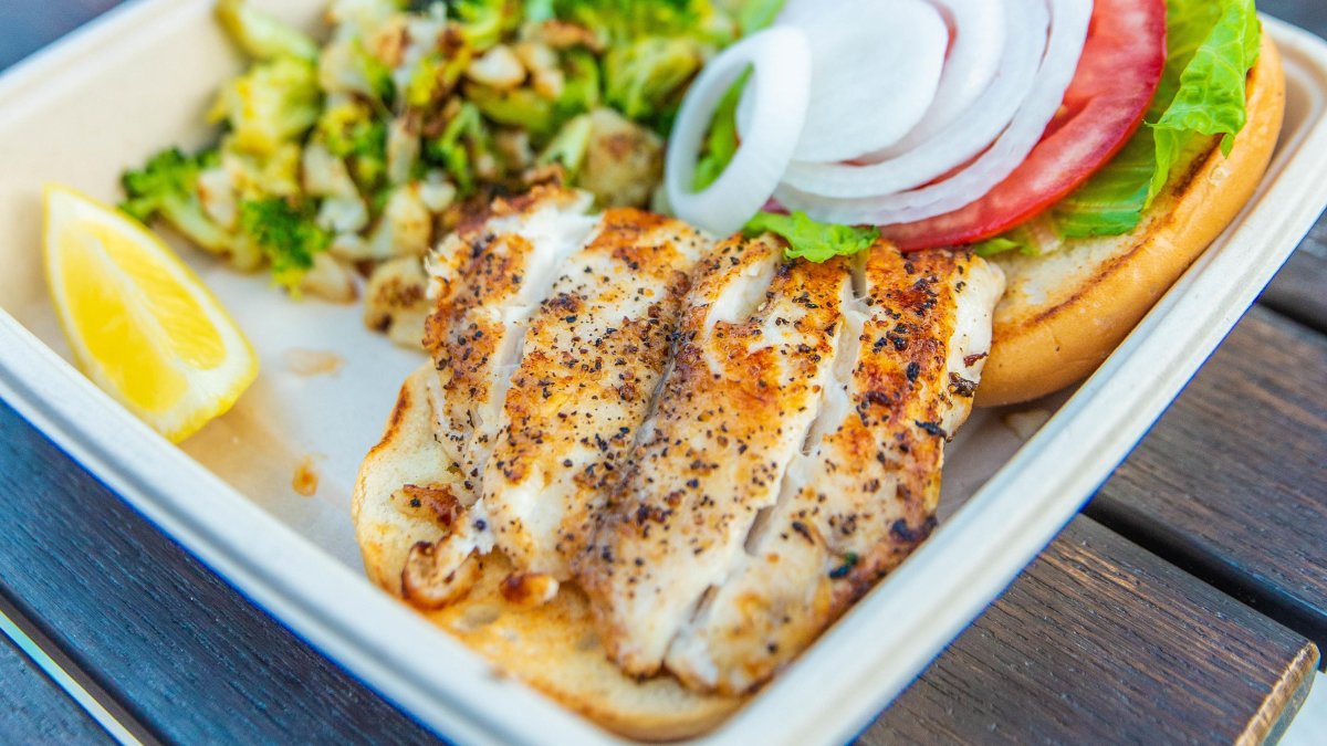 A close view of a grouper fish plate with onions, tomatoes and green vegetables.