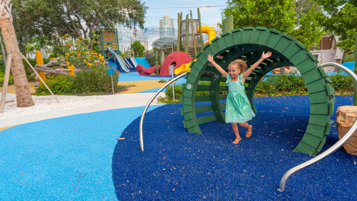 A little girl dressed in green dress, with arms wide open while going through a tunnel at St. Pete Pier playground.