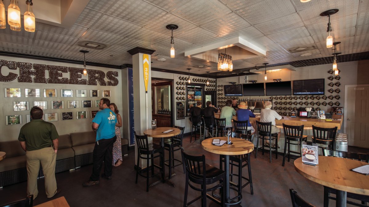 The interior of Sea Dog Brewing showing few people at the bar and tall tables with chairs.