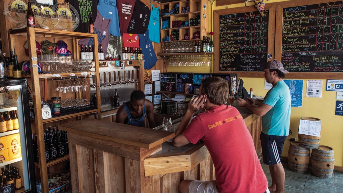 The interior view of 7venth Sun Brewery showing two people ordering drinks and lots of merchandising for sale.