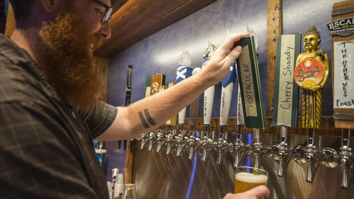 A long-bearded man pouring beer from the tap. 