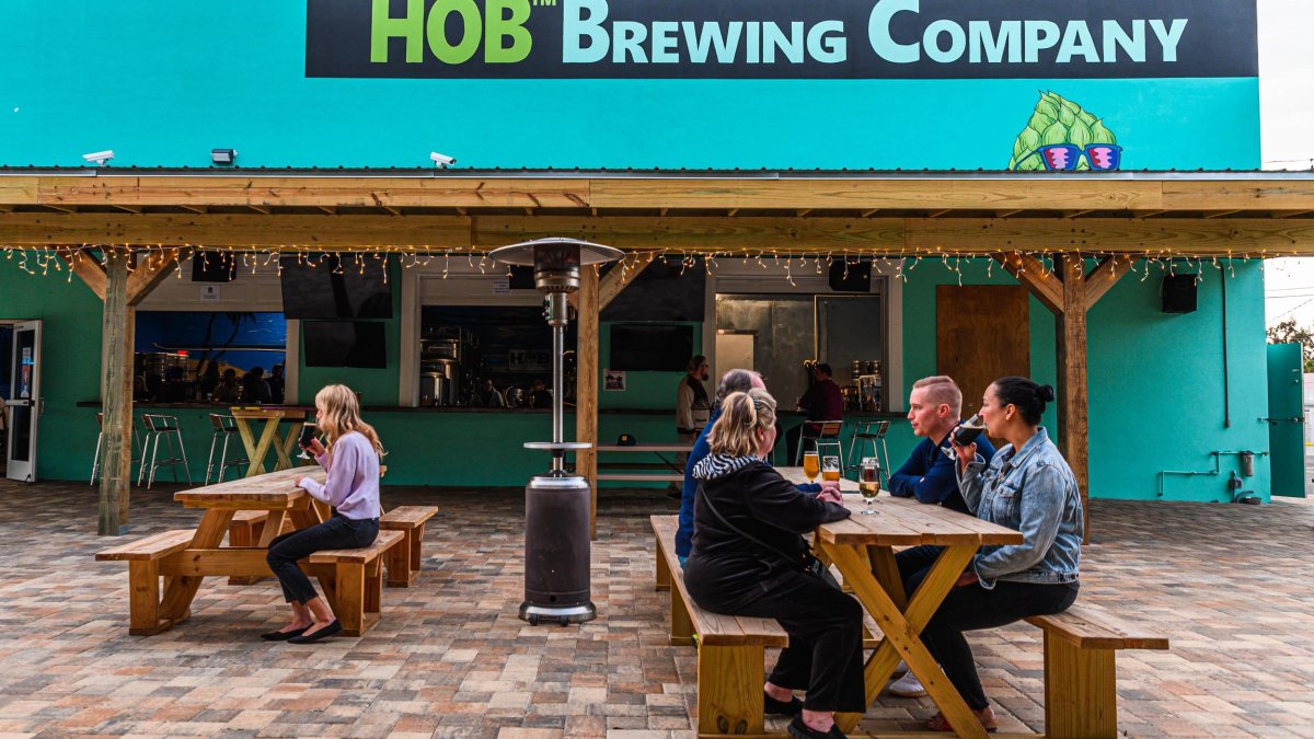 Several people enjoying beers outside of the HOB Brewing Co., seating on wooden benches.