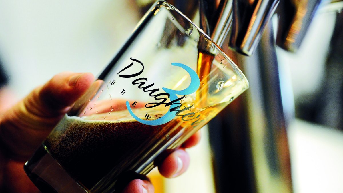 A person pouring dark beer in a 3 Daughters Brewery glass.