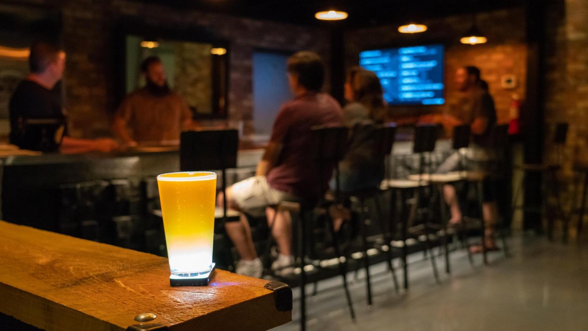 A beer glass on top of the bar and few people enjoying drinks at Avid Brewing Co.