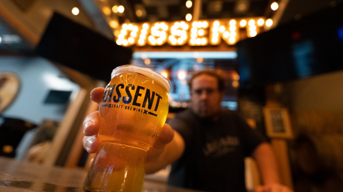 A man holding a glass of beer. A big sign saying "Dissent" is on display.