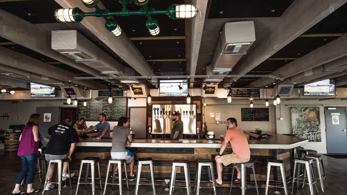 The interior view of de Bine Brewing showing tall seats by the bar and people drinking beer.