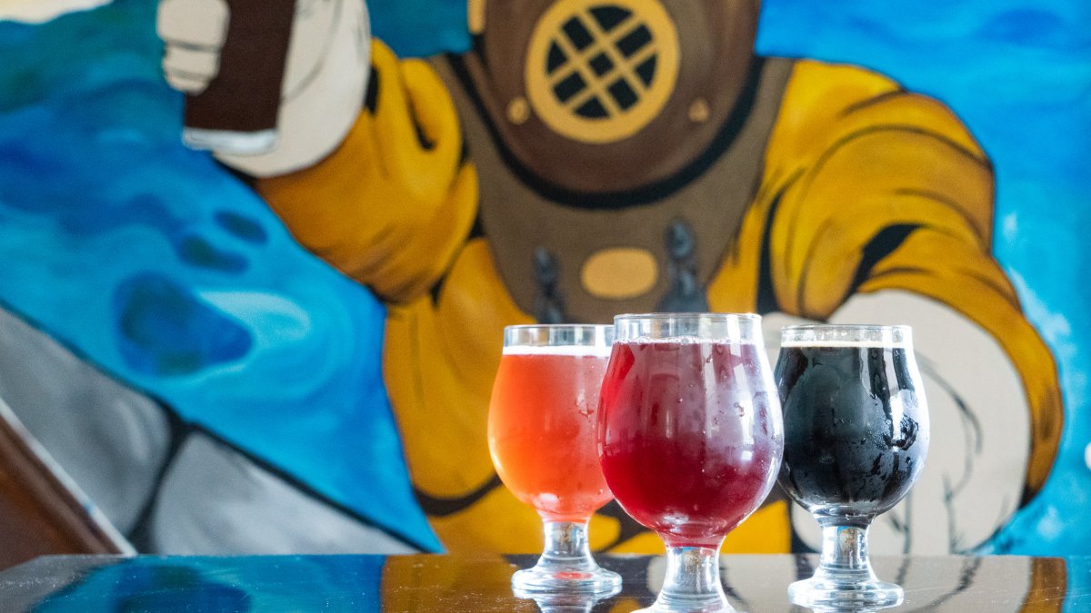 Three round beer glasses in front of a mural of a sponge diver.