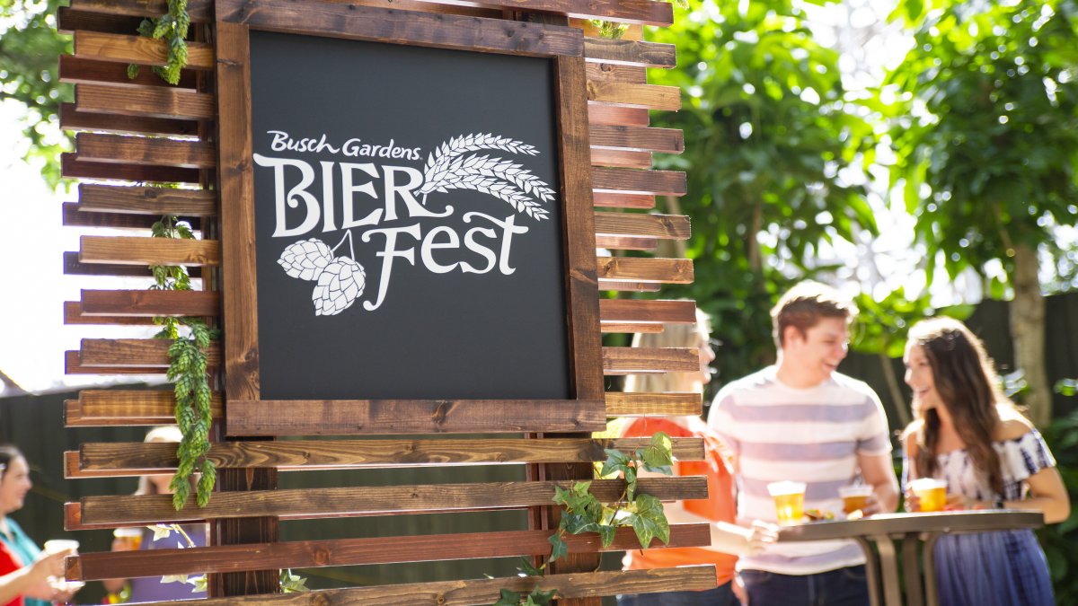 A man and woman at a cocktail table with the Busch Gardens Bier Fest sign in the background