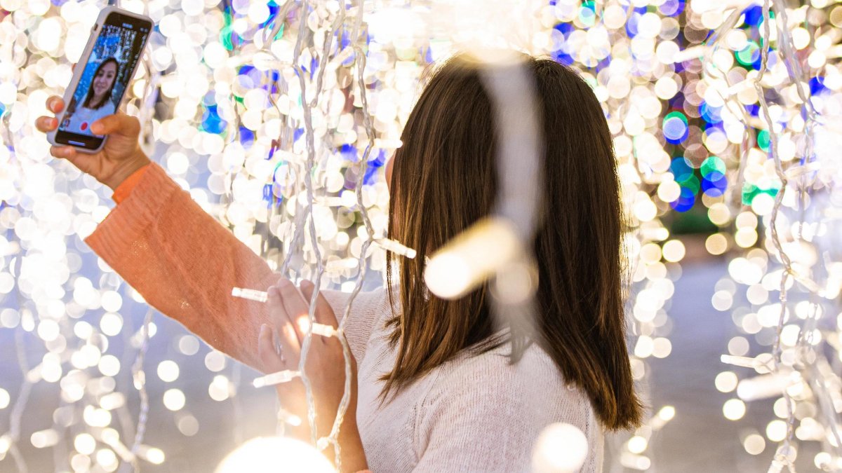 A woman takes a selfie with Christmas lights all around at Enchant Christmas