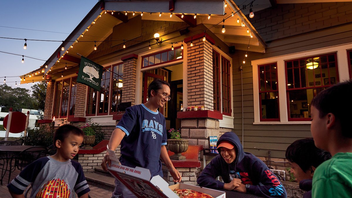 A man serves a large pizza to a group outside of Cappy's Pizza in St. Pete