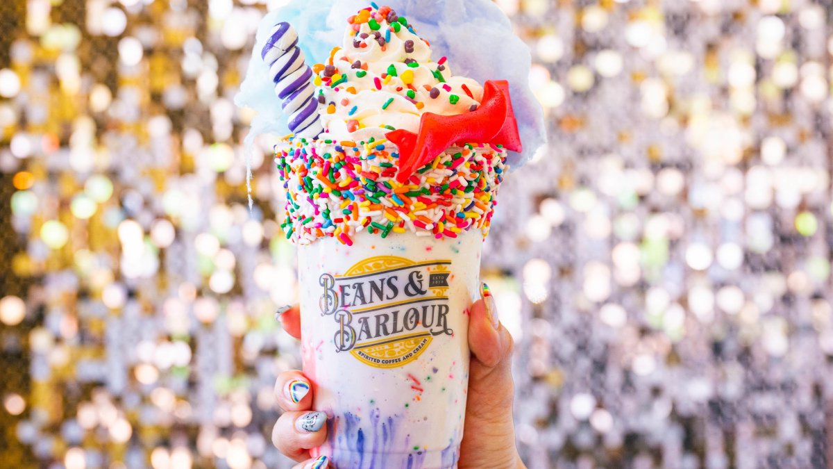 A milkshake overflows with rainbow sprinkles, a chocolate-covered pretzel rod and other sweets.