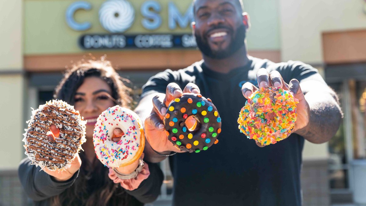 Two people hold up elaborate, colorful donuts