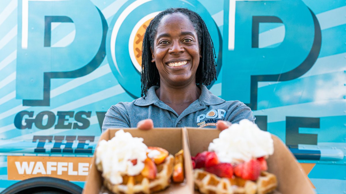 A woman holds up two waffles covered with fruit, whipped cream and other toppings