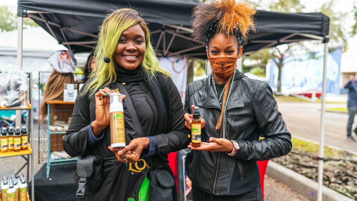 Two young women hold up products from a vendor at an outdoor event.