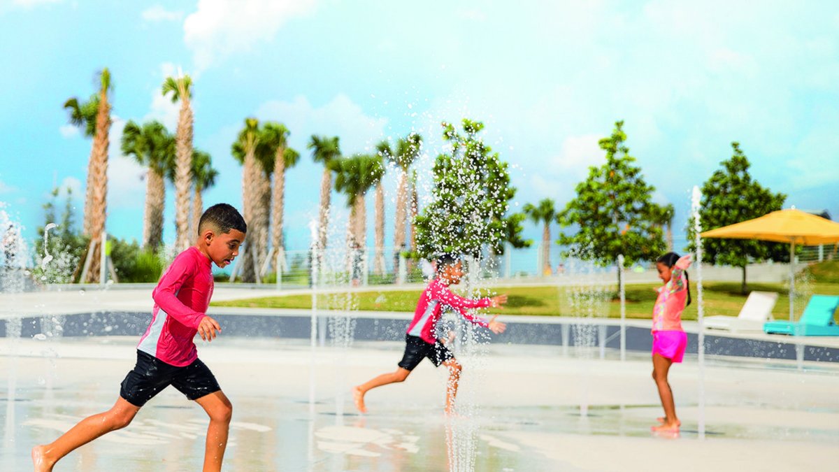 Três crianças brincam no splash pad do St. Pete Pier com palmeiras ao fundo